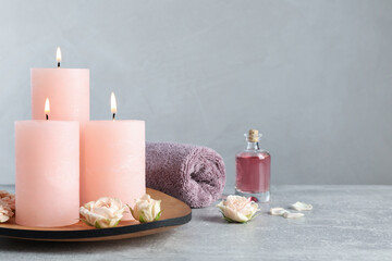 Obraz na płótnie Canvas Burning candles, roses, essential oil and towel on grey table