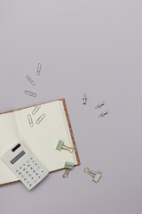 Back to school creative concept. Study or office workplace with stationary like notebook,  calculator and clips on a purple paper background.  Minimalistic flat lay, top view with copy space.