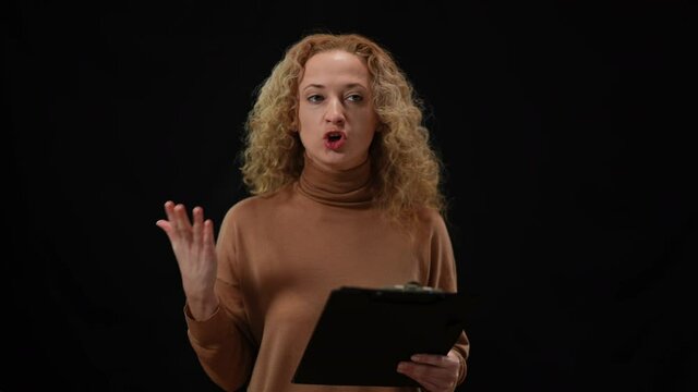 Emotional Caucasian woman talking gesturing standing at black background. Portrait of agitated female speaker presenting manifest at press conference. Confidence and public lifestyle