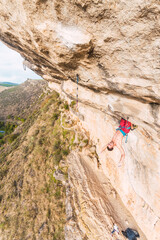 Aerial view of a climber clinging with his legs on the rock.