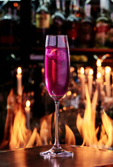 Purple cocktail with glitter in a glass for champagne on copper designer bar counter, the background of real fire. close up. . High quality photo