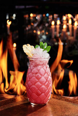 beautiful serve of a pink cocktail with crash, decorated with mint and pineapple slice on copper plates against the background on the real fire. close up. High quality photo