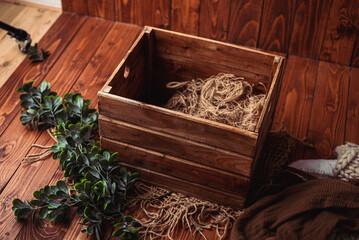 Basket on a wooden floor. Props for newborn photography. Brown basket with dark green branch 