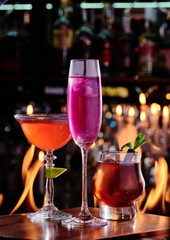 Three colorful cocktails in beautiful glasses against a background of real fire. Space for text. High quality photo