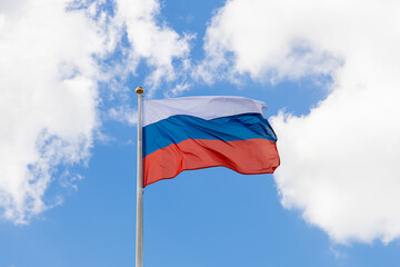 Waving Russian tricolor. The flag of Russia flutters in the wind on a sunny day. Flag of the Russian Federation on a pole against the sky with clouds. Tricolor - state symbol of Russia