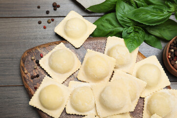 Uncooked ravioli, basil and peppercorns on wooden table, closeup