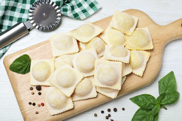 Uncooked ravioli with basil and peppercorns on white wooden table, flat lay