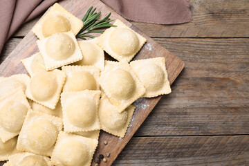 Uncooked ravioli and rosemary on wooden table, flat lay. Space for text