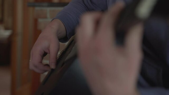 Authentic man play on wooden acoustical guitar changing accords sitting on sofa at home close view