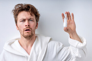 Closeup of young man in bathrobe with sickness using nasal spray for congested nose. Sick man using...