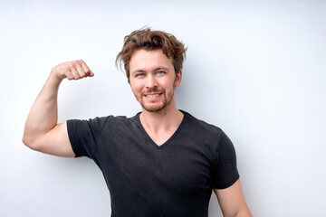 muscular man in casual wear shows muscles on arms, feels proud to be strong and have strength. I am hero. Successful smiling male model raises hands with joy, shows great power. Healthy lifestyle