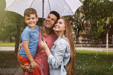 Happy family with umbrella walking under rain in park © New Africa