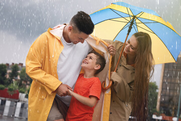 Happy family with umbrella walking under rain on city street