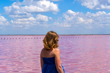 Happy beautiful girl in blue long dress standing in water on pink salt lake on sunny summer day. Wanderlust travel concept