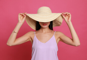 Beautiful young woman with straw hat on pink background