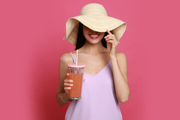Beautiful young woman with straw hat and glass of refreshing drink on pink background