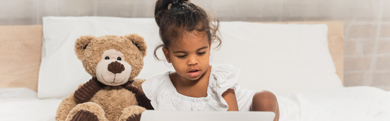 african american kid watching movie on laptop near soft toy, banner