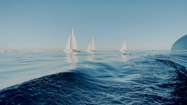 View of sailing race from a judicial rubber motor boat, some sailboats in a list goes by sea, the clear sky, sail regatta, reflection of sail on the water