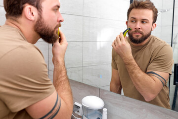 beauty, shaving, grooming and people concept. handsome man looking at mirror, shaving beard with...