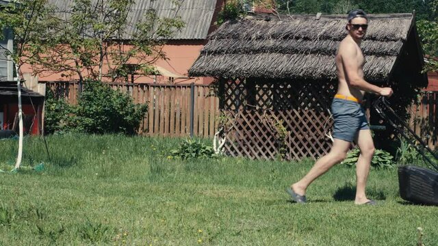 Man walk behind or push petrol lawnmower in backyard. Cutting grass by self propelled mower with rear roller and grass catcher. Garden or agricultural machine to cut grass surface with mulching blade
