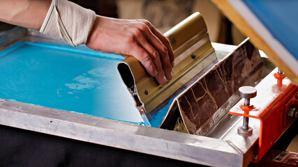 selective focus photo of male hand with a squeegee. serigraphy production. printing images on...