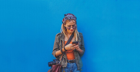Young girl standing by the blue background holding a smartphone - A hipster stylish girly smiling...