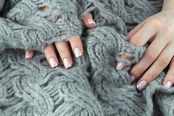 Female hands with beautiful stylish french manicure touching warm knitted blanket.