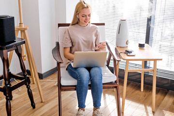 working at home, smart working. blonde caucasian woman using laptop and more technological devices for communicate and work, in smart house. copy space