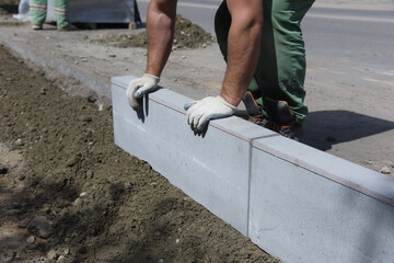 A worker aligns a road curb installed in cement with his hands,the construction of a new highway.