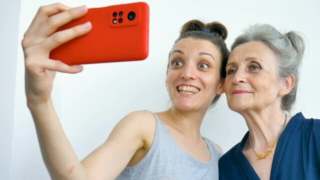 Adult daughter and senior mum are taking self-portrait picture, selfie on red smartphone together, happy retirement, mothers day concepts.