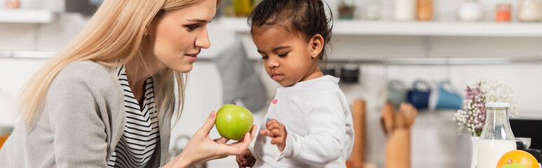mother giving apple to adopted african american kid in kitchen, banner