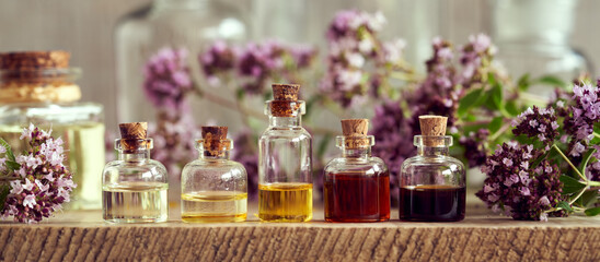 Panoramic header of essential oil bottles with blooming oregano plant. Aromatherapy or alternative medicine.