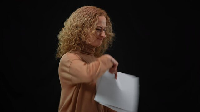 Nervous Caucasian woman throwing away paperwork rehearsing speech at black background. Side view portrait of anxious troubled spokesperson crossing hands looking away