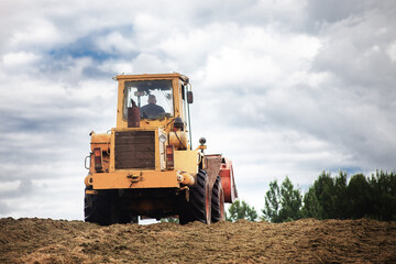 A yellow bulldozer at work, high on a hill against a dramatic sky.