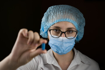girl doctor in a mask and white coat holding a blue capsule pill in her hands