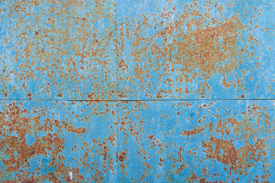 The wall, lined with old iron sheets, looks like a geographical map. There are many patches of rust and remains of blue paint. Background. Texture.