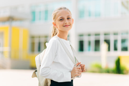 Primary school student, girl with a backpack near the building outdoors, Start of lessons, The first day of autumn.