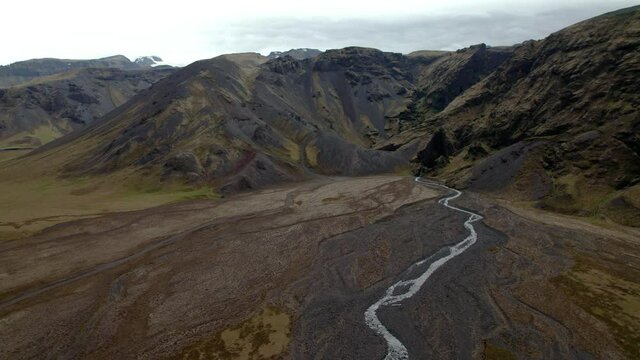 Aerial shot slowly rising, epic view of mountains in Iceland with creek below. Overcast day, shot in summer.