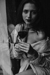 Beautiful woman looking into camera and holding wine glass. Black and white portrait of charming lady posing in bar
