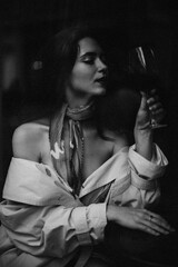 Portrait of attractive lady with wine glass. Black and white photo of young woman in stylish trench coat drinking champagne