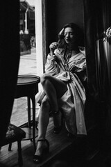 Fototapeta na wymiar Elegant lady resting in bar with wine glass. Black and white portrait of young beautiful woman dressed in trench coat