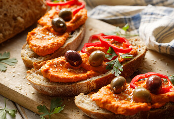 Sourdough bread sandwiches with paprika hummus, olives, slices of red pepper and herbs close up view. Vegetarian food concept