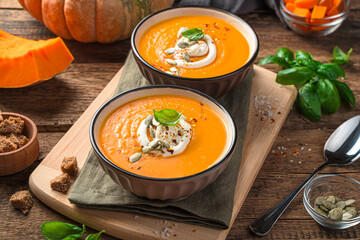Two servings of pumpkin cream soup with cream on a wooden background. Side view.