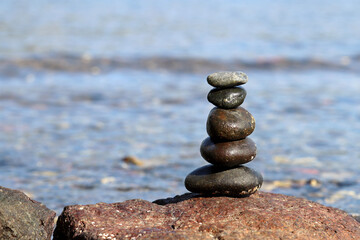 Fototapeta na wymiar Pyramid of pebbles on blurred background of the sea waves. Summer vacation, balance and relax concept