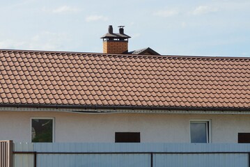  private gray house with windows under a brown tiled roof against a sky behind a fence 