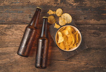Obraz na płótnie Canvas Dark beer bottles and chips in a bowl on a wooden background.