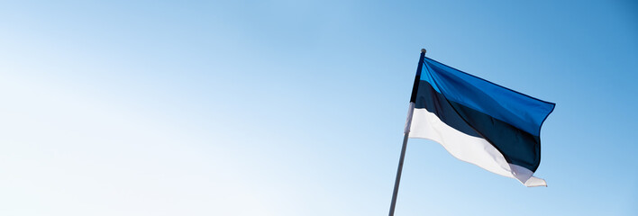 Estonian flag waving in wind and sunlight. Flag of Estonia on blue sky background. Empty copy space...