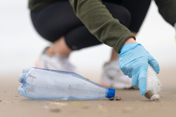 A volunteer in blue gloves removes rubbish, plastic bottles. Focusing on the foreground. Macro photography. Environmental pollution control problems.
