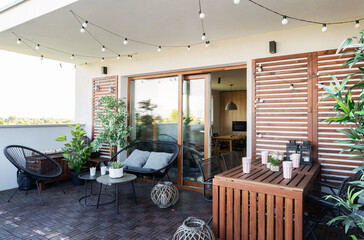 Terrace outside the house with plants, wooden wall and table, comfortable sofa and stylish lamps....