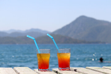 Two glasses with cocktail on a wooden pier on sea and mountains background. Summer vacation on a...